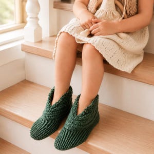 Può includere: Un paio di pantofole in maglia verde bosco scuro caratterizzate da un motivo a coste testurizzato e un design incrociato alla caviglia. Le pantofole sono realizzate con una lavorazione a filo spesso, con punta arrotondata e vestibilità.