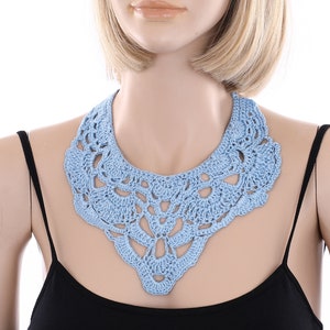 May include: A light blue crocheted collar necklace. The necklace is made of delicate, intricate stitches and has a scalloped edge.
