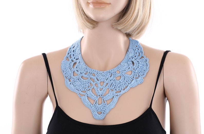 May include: A light blue crocheted collar necklace. The necklace is made of delicate, intricate stitches and has a scalloped edge.