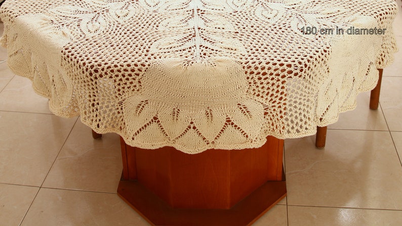 Puede incluir: Un mantel de crochet de color crema con un delicado patr&oacute;n floral. El mantel est&aacute; puesto sobre una mesa de madera con un di&aacute;metro de 480 cm.