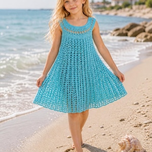 Peut inclure: Robe turquoise en crochet, col rond et sans manches. La robe présente une jupe évasée et est portée par une personne sur une plage de sable. Un coquillage et une étoile de mer sont sur le sable près de la personne.