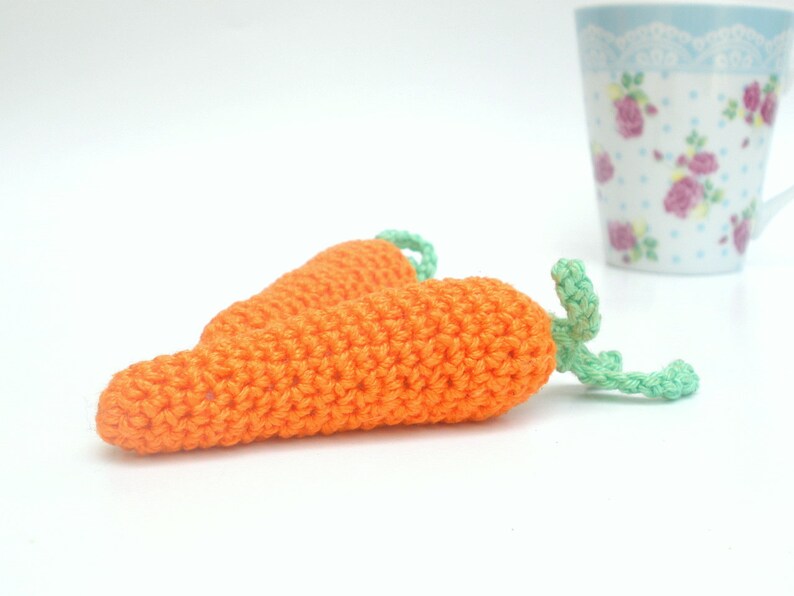 May include: Two crocheted carrots with green tops. The carrots are orange and the tops are a light green.