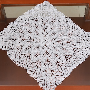 May include: A white crocheted doily with a delicate, intricate pattern. The doily is square shaped and has a circular design in the center.