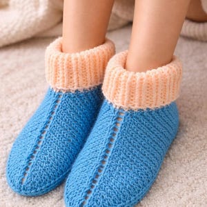 Könnte beinhalten: Ein Paar handgestrickte blaue Hausschuhe mit pfirsichfarbenen Bündchen. Die Hausschuhe haben ein strukturiertes Strickmuster und einen dekorativen Schlitz. Ideal für den Innenbereich.