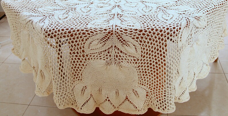 Puede incluir: Un mantel de mesa de ganchillo blanco con un delicado patr&oacute;n floral. El mantel es redondo y tiene un borde festoneado.