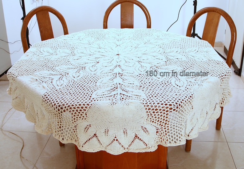 Puede incluir: Un mantel de crochet blanco con un delicado patr&oacute;n floral. El mantel tiene 180 cm de di&aacute;metro y est&aacute; colocado sobre una mesa de madera con tres sillas.
