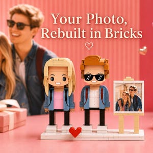 May include: A custom brick-built display featuring two stylized figures standing on a white base with a small red heart. Next to the figures is a miniature easel holding a photograph. The text above reads: Your Photo, Rebuilt in Bricks.