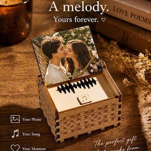 Könnte beinhalten: Eine Holz-Spieluhr mit einem Foto eines sich küssenden Paares. Die Box hat ein dekoratives Design und der Text "A memory. A melody. Yours forever." wird angezeigt. Die Box hat auch den Text "Your Photo", "Your Song" und "Your Moment".