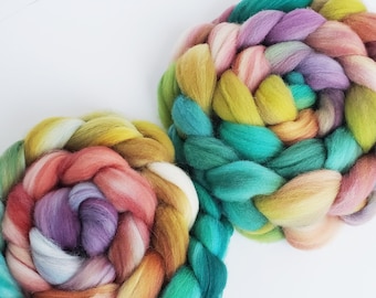 Könnte beinhalten: Zwei bunte Wollgarne, geflochten und zu einer Spirale gedreht. Die Garne sind eine Mischung aus Grün, Gelb, Rosa und Lila.