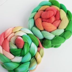 May include: Two colorful rovings of wool yarn in shades of green, pink, and yellow, braided into a flower shape.