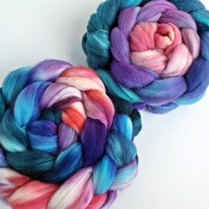 May include: Two colorful braided yarn skeins. The yarn features a gradient of colors, including teal, blue, purple, pink, and orange. The skeins are arranged on a white background, showcasing the vibrant hues and textures of the fiber.