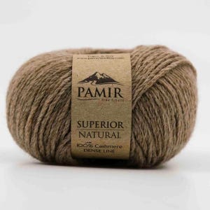 Könnte beinhalten: Ein Knäuel braunes Garn mit einem Etikett, auf dem "PAMIR fine fibers SUPERIOR NATURAL 100% Cashmere DENSE LINE" steht. Das Etikett zeigt eine Berg-Grafik. Das Garn ist dicht gewickelt und wirkt weich.
