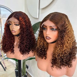 May include: Two mannequin heads showcasing curly wigs. The wig on the left is a deep auburn with copper highlights. The wig on the right is a blend of brown and blonde. Both wigs feature a lace front and are styled with voluminous curls.