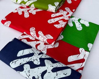 May include: Folded fabric in red, green, and navy blue, each with a white, abstract pattern. The fabric is neatly stacked, showcasing the contrasting colors and design. The overall theme suggests textiles or decorative items.