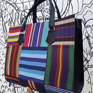 May include: A patchwork tote bag with a variety of colorful striped and patterned fabric panels. The bag has black handles and accents, with a rectangular shape. The background features a black and white illustration.