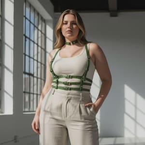 Może przedstawiać: Kobieta nosi zieloną skórzaną uprząż i choker na białym topie, w połączeniu z beżowymi spodniami z szerokimi nogawkami. Uprząż posiada wiele pasków i srebrne klamry. Strój jest stylizowany w jasnym, nowoczesnym otoczeniu.