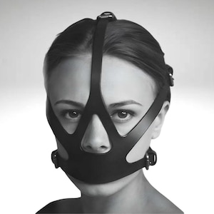 May include: A black leather face mask with a unique design, featuring straps that secure around the head and face. The mask covers the nose and mouth area, with openings for the eyes. The image is in black and white.