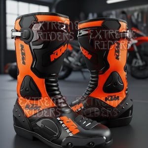 Könnte beinhalten: Paar schwarze und orangefarbene Motorradstiefel mit dem KTM-Logo. Die Stiefel haben ein hohes Design mit mehreren Schnallen und Schutzplatten. Der Text "EXTREME RIDERS" ist auf den Stiefeln zu sehen.