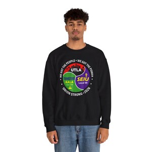 May include: Black sweatshirt with a circular graphic featuring the text "WE GOT THE PEOPLE" and "WE GOT THE POWER." The graphic includes the text "UTLA," "TEAMSTERS AALA Local 2010," and "SEIU Local 99." The words "UNION STRONG 2026" are also present.