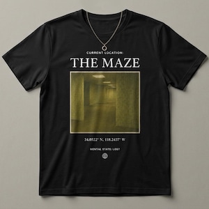 Könnte beinhalten: Schwarzes T-Shirt mit einer goldenen Halskette. Das Shirt zeigt den Text "THE MAZE" über einem rechteckigen Bild eines langen, gelb beleuchteten Flurs. Darunter stehen Koordinaten und die Worte "MENTAL STATE: LOST."