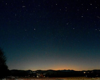 May include: A dark night sky with a vast expanse of stars visible. The horizon is a dark silhouette of hills and trees.