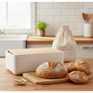 May include: A white bread box with a bamboo lid, a wooden breadboard, and several loaves of bread. A canvas bag with the text "LIBKEN SUSTAINABLE HOUSEWARE" is behind the bread box. The scene is set on a wooden countertop.
