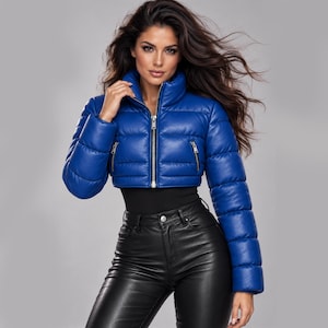 May include: A cropped, royal blue puffer jacket with a high collar, long sleeves, and a front zip fastening. The jacket features horizontal quilted stitching and two side pockets with silver-toned metal zips, worn over a black top and trousers.