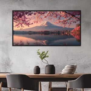 May include: A framed landscape print featuring Mount Fuji with a snow-capped peak, reflected in a calm lake. Cherry blossoms in shades of pink and red frame the mountain, with a village at the base.