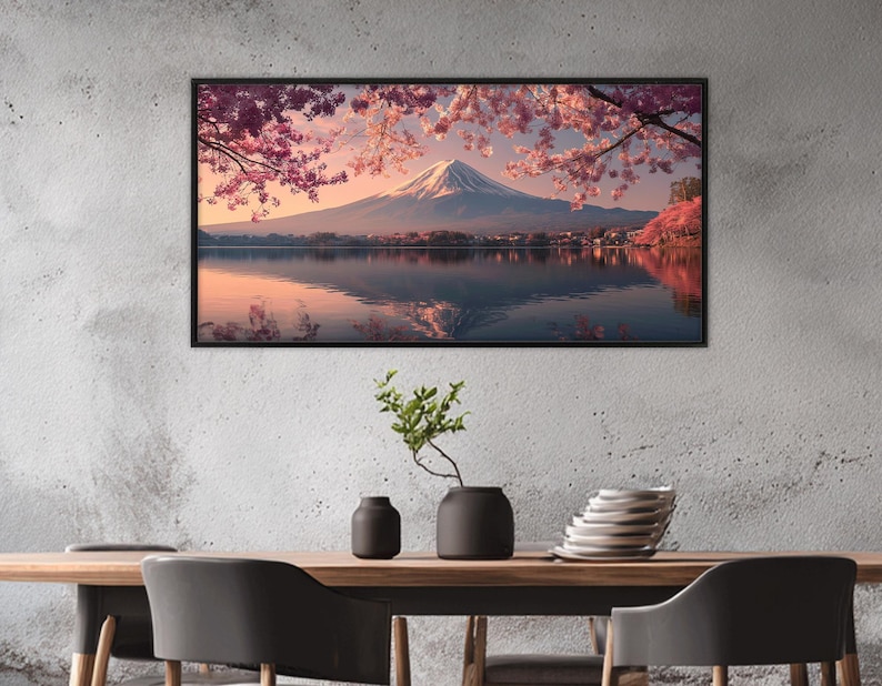 May include: A framed landscape print featuring Mount Fuji with a snow-capped peak, reflected in a calm lake. Cherry blossoms in shades of pink and red frame the mountain, with a village at the base.