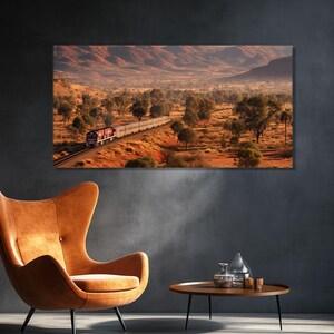 May include: A large rectangular canvas print depicts a train traveling through a desert landscape. The train is red and white, and the landscape features red-orange soil, green trees, and distant mountains. The print is displayed on a dark gray wall.