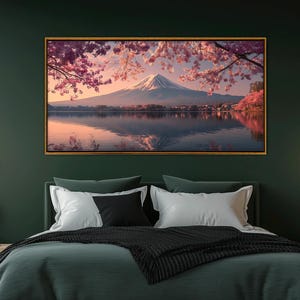 May include: A framed landscape print featuring Mount Fuji reflected in a lake, under a sky with pink cherry blossoms. The artwork has a gold frame and is displayed above a bed with green bedding.