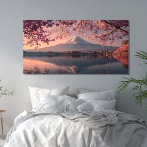 May include: A canvas print of a serene landscape featuring a snow-capped mountain reflected in calm water. Pink cherry blossoms frame the scene, with a soft, warm color palette. The artwork is displayed above a bed with white linens.