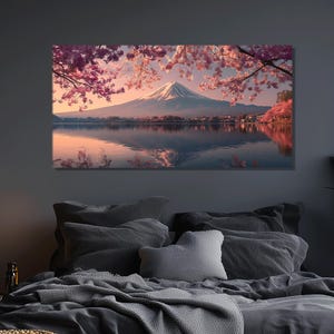 May include: A canvas print of a serene landscape featuring a snow-capped mountain reflected in a calm lake. Pink cherry blossoms frame the scene, with a soft, warm color palette. The artwork is displayed above a bed with gray bedding.