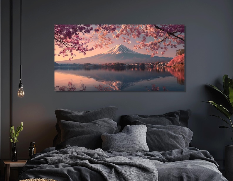 May include: A canvas print of a serene landscape featuring a snow-capped mountain reflected in a calm lake. Pink cherry blossoms frame the scene, with a soft, warm color palette. The artwork is displayed above a bed with gray bedding.