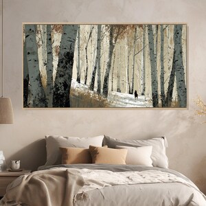 May include: A framed art print showcases a winter forest scene. The artwork features tall birch trees with black and white bark, lining a snow-covered path. A figure walks in the distance. The print is in a natural wood frame, complementing the neutral colour palette.