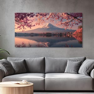 May include: A large rectangular canvas print depicting Mount Fuji reflected in a lake. Pink cherry blossoms frame the snow-capped mountain. The artwork is displayed above a gray sofa in a living room.