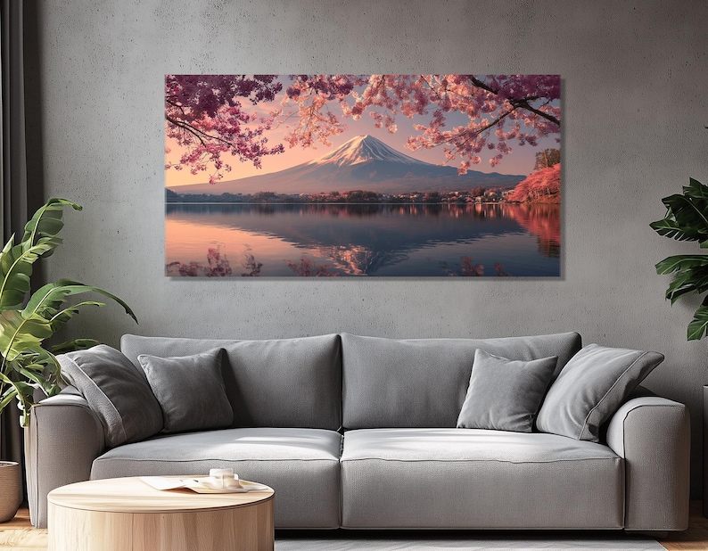 May include: A large rectangular canvas print depicting Mount Fuji reflected in a lake. Pink cherry blossoms frame the snow-capped mountain. The artwork is displayed above a gray sofa in a living room.
