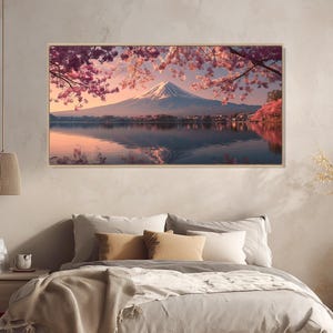 May include: A framed landscape print featuring Mount Fuji reflected in a lake, under pink cherry blossoms. The artwork has a serene, natural theme, with a color palette of pink, blue, and white. The print is displayed above a bed.