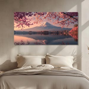 May include: A canvas print of Mount Fuji reflected in a lake, framed by pink cherry blossoms. The snow-capped mountain is set against a soft, pastel sky. The artwork is displayed above a bed with neutral-toned bedding.