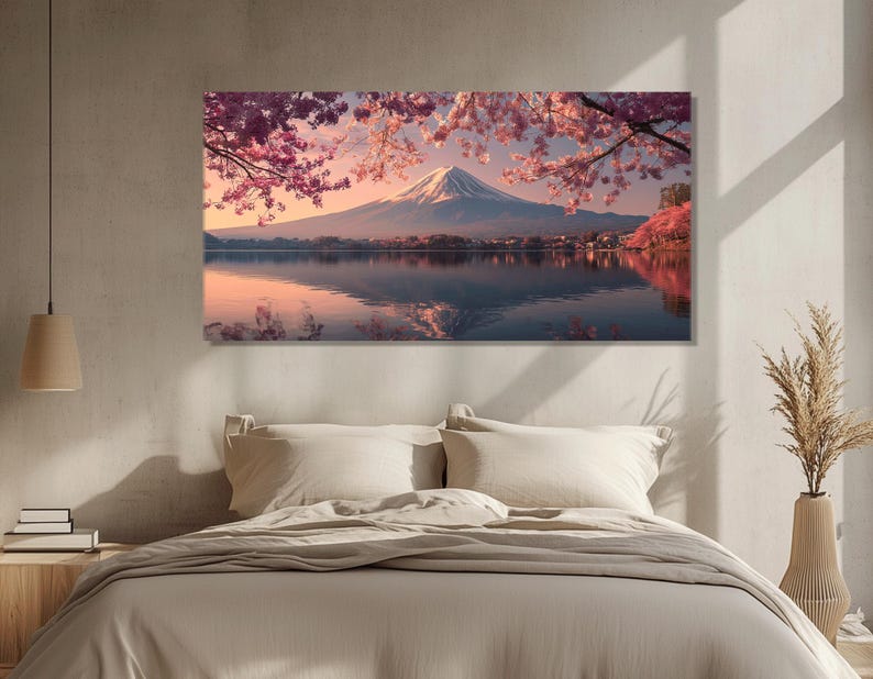 May include: A canvas print of Mount Fuji reflected in a lake, framed by pink cherry blossoms. The snow-capped mountain is set against a soft, pastel sky. The artwork is displayed above a bed with neutral-toned bedding.