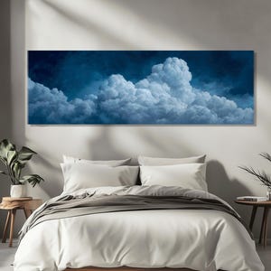 Puede incluir: Una impresión rectangular en lienzo que representa un paisaje de nubes. La obra presenta nubes blancas y esponjosas contra un cielo azul oscuro. La impresión está montada sobre una cama con ropa de cama blanca, creando una escena de dormitorio serena.