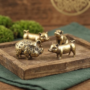 May include: A collection of four small brass pig figurines with a metallic gold finish. One pig features a textured, bumpy surface, while the other three have smooth, polished surfaces. Each figurine depicts a pig in a standing or sitting pose.