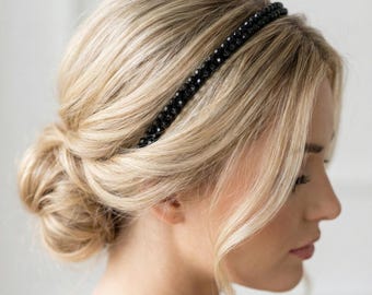 Puede incluir: Una diadema negra con cuentas usada por una persona con cabello rubio peinado en un moño bajo. La diadema es delgada y presenta pequeñas cuentas oscuras. El cabello está peinado con mechones sueltos que enmarcan la cara.