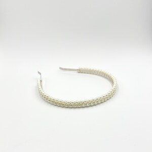 May include: A pearl beaded headband with a silver metal band. The headband is adorned with two rows of small, round, off-white pearls. The design is simple and elegant, suitable for various occasions.