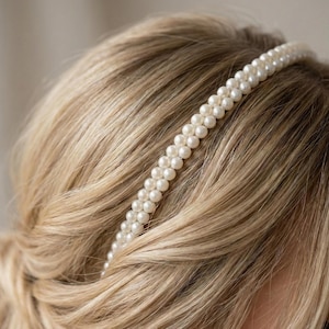 May include: A double-strand pearl headband, with small, round, off-white pearls. The headband is set against a backdrop of blonde hair, creating a classic and elegant look. Ideal for weddings or special occasions.