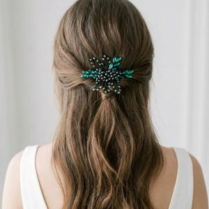 Könnte beinhalten: Nahaufnahme einer Frisur mit einer dekorativen Haarspange. Die Spange hat ein sternförmiges Design mit dunkelgrünen und klaren Kristallakzenten. Das Haar ist braun und die Frau trägt ein weißes Oberteil.