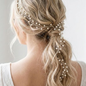 Puede incluir: Un delicado accesorio para el cabello de novia con una vid de alambre plateado adornada con pequeñas perlas blancas redondas. La vid está dispuesta en el cabello, creando un aspecto elegante y romántico. El cabello es rubio y peinado en una cola de caballo baja.