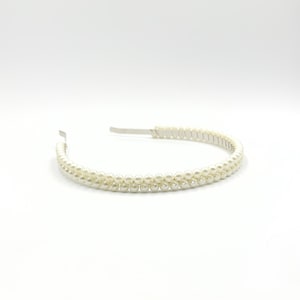 May include: A white faux pearl headband. The headband has two rows of small, round, off-white pearls. The band is made of silver-coloured metal. The pearls are evenly spaced, creating a delicate and elegant appearance.