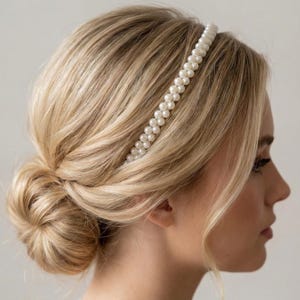 May include: A double-strand pearl headband on a person with blonde hair styled in a low bun. The white pearls are evenly spaced, creating a classic and elegant look. The hair is styled with a side parting.