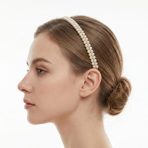May include: A double-strand pearl headband. The hair accessory is made of small, round, off-white pearls. The headband is worn on the head. The hair is pulled back in a bun against a light background.